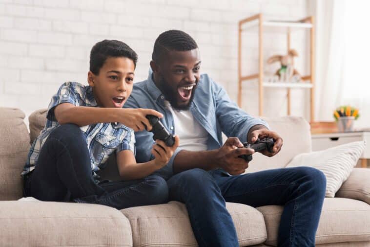 père enfant jouant jeu VR sans casque sur canapé