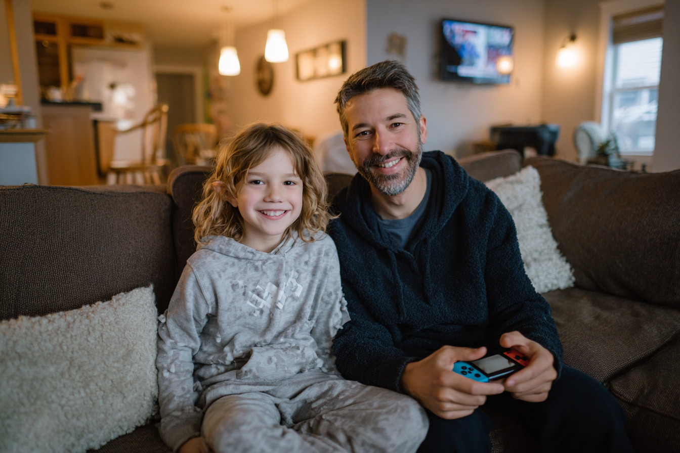Un parent et son enfant jouent ensemble à la Nintendo Switch dans un salon cosy à l’éclairage chaleureux, illustrant le côté familial et relaxant de Pokémon Friends.