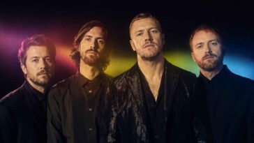 Les quatre membres du groupe rock posent en vêtements sombres, éclairés par des halos de lumière violette, jaune et bleue.